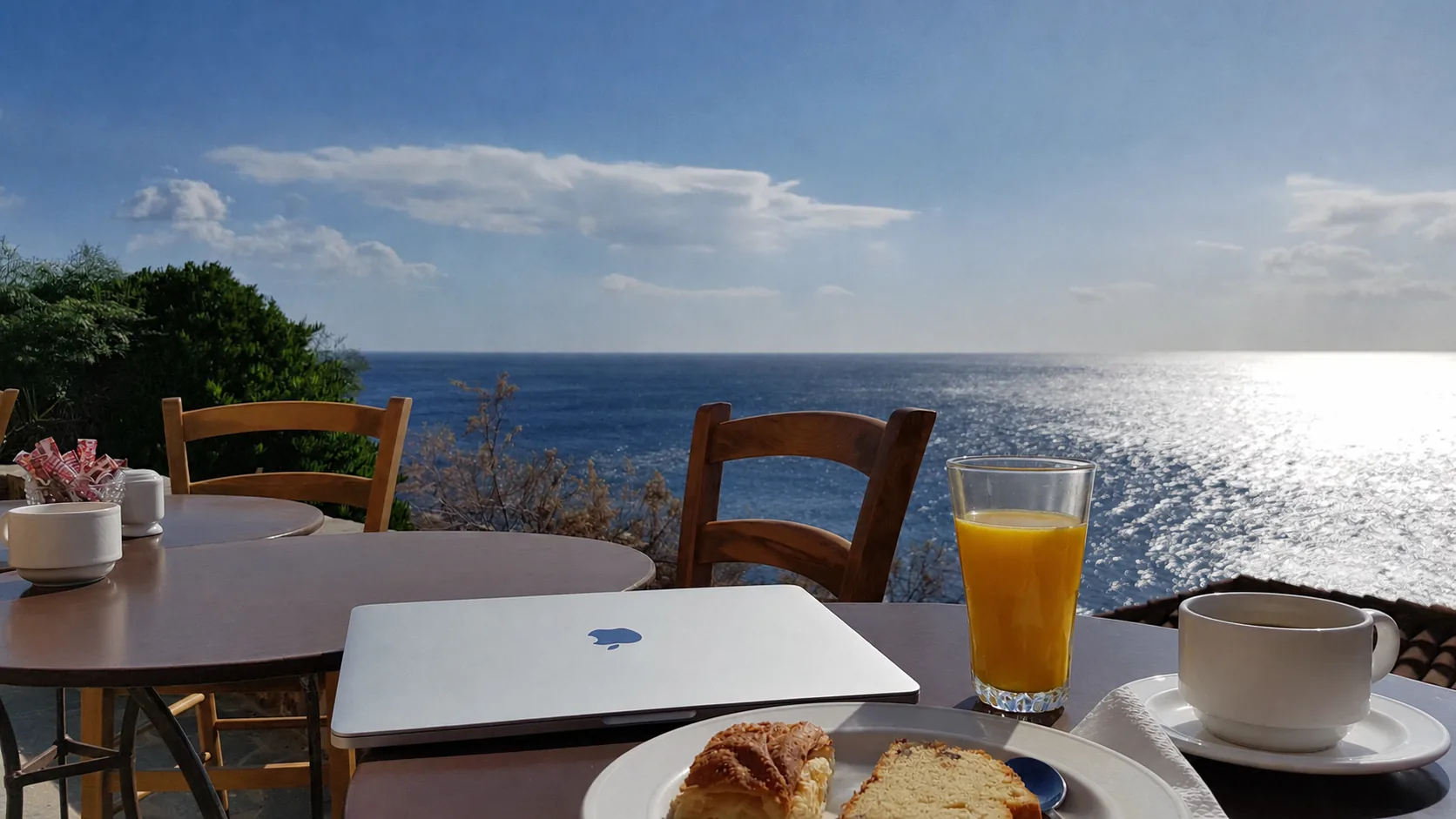 Tisch mit Laptop, Kaffee und Orangensaft vor dem Meer